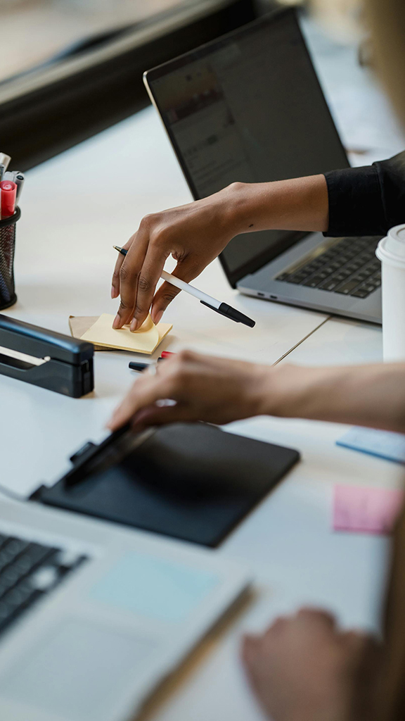 Close-up of hands using office supplies on a desk with laptops