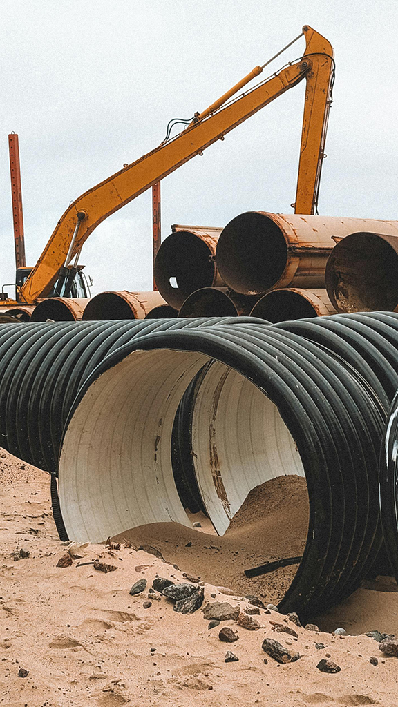 Large black corrugated pipes and rusty metal pipes at construction site.
